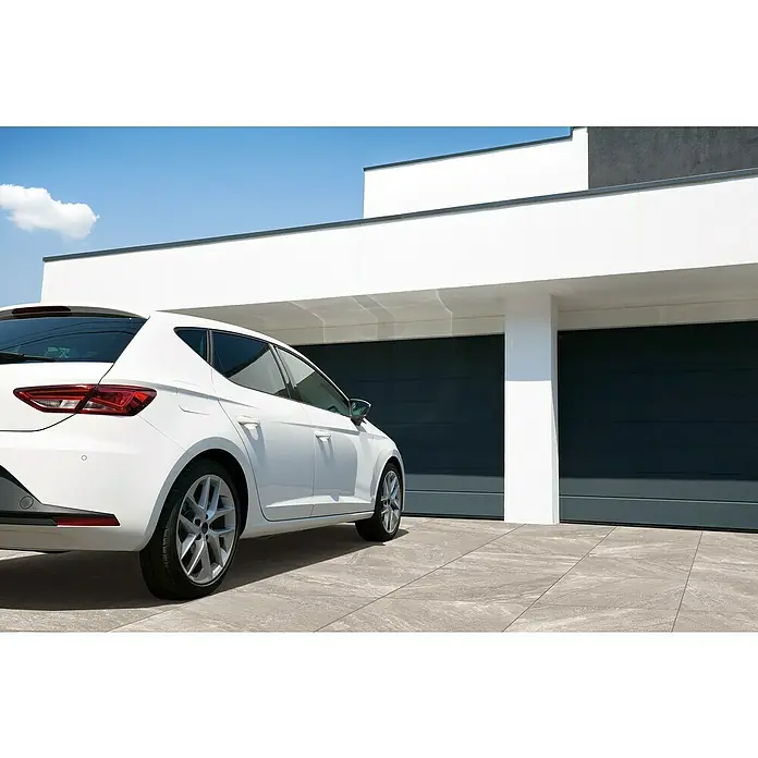Terrassenfliese Cera 2.0 - 80 x 80 x 2 cm, Quarz Grigio, Matt - Moderne Garage mit einem weißen Auto davor. Die Garage hat zwei graue Tore und ein flaches Dach. Das Auto ist ein Seat Leon in Weiß.