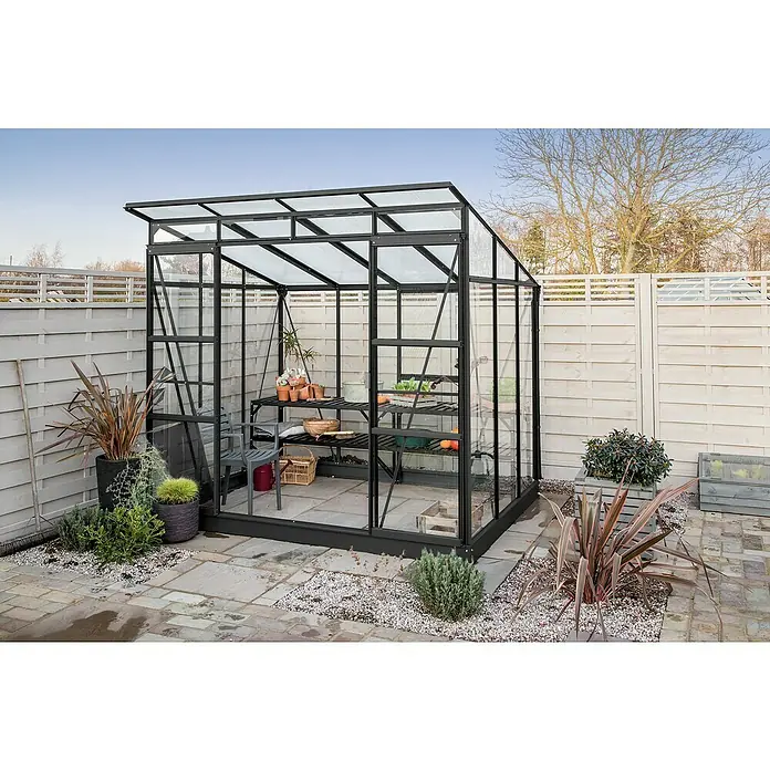 Vitavia Gewächshaus Freya 5900 Plus - Außenmaß inkl. Dachüberstand (B x T): 229 x 258 cm, Wandstärke: 3 mm, Schwarz - Ein modernes Gewächshaus mit schwarzem Rahmen und klaren Scheiben, umgeben von Pflanzen und einem gepflasterten Bereich.