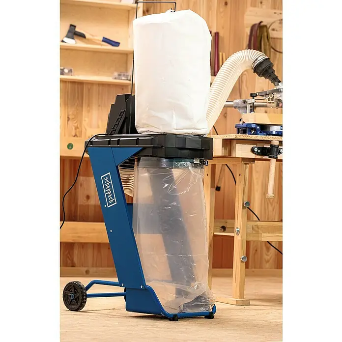 Scheppach Absauganlage DC500 - 550 W, Staubbeutelvolumen: 75 l - Das Bild zeigt einen Scheppach-Absauganlage mit einem blauen Gehäuse, einem weißen Filtersack und einem transparenten Auffangsack in einer Werkstatt.