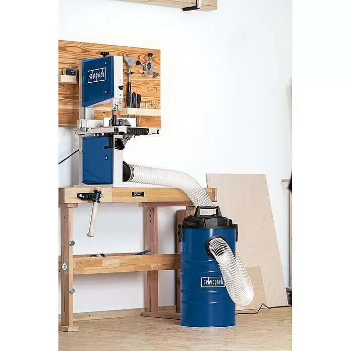 Scheppach Absauganlage DC100 - Luftleistung: 215 m³/h, 65 l, 1.200 W - Blaue Scheppach Bandsäge auf einer Holzwerkbank, verbunden mit einem blauen Scheppach Staubsammler mit transparentem Schlauch in einer Werkstatt.