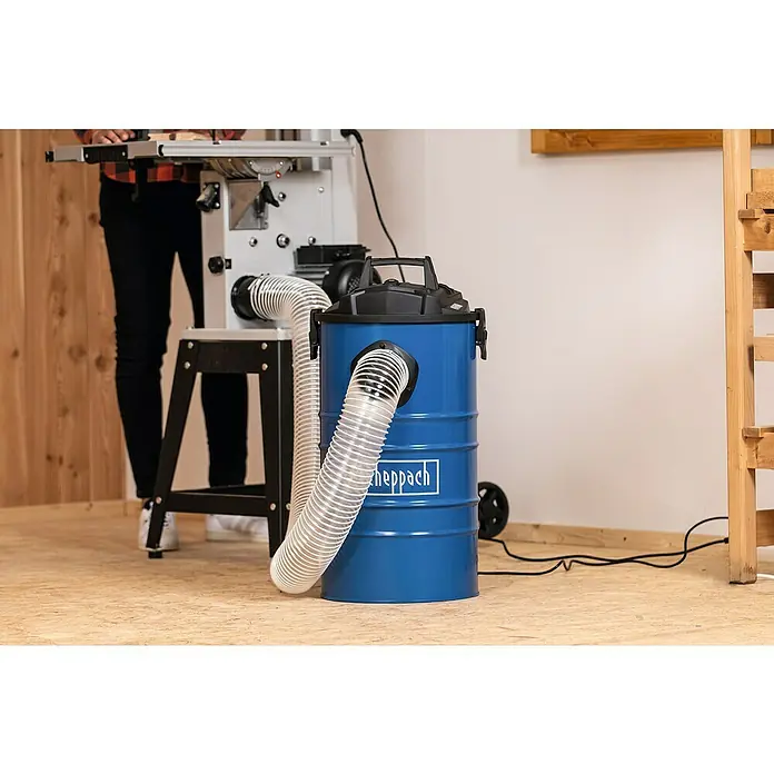 Scheppach Absauganlage DC100 - Luftleistung: 215 m³/h, 65 l, 1.200 W - Der blaue Scheppach-Werkstattsauger mit Schlauch ist an eine Werkbank angeschlossen, um Staub und Späne abzusaugen.