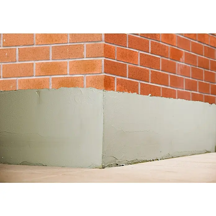 Ultrament Reaktivabdichtung Easy Dicht - 10 kg, 1-komponentig - Nahaufnahme einer frisch verputzten Außenwand mit einem Sockel, der das Mauerwerk vor Feuchtigkeit schützt und das Erscheinungsbild verbessert.
