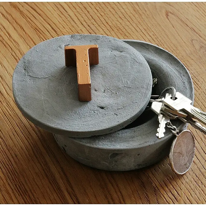 Ultrament Beton-Knetmasse Knet Beton - Hellgrau, 2,5 kg - Runde Betonbox mit Deckel und einem bronzefarbenen "T" darauf, ideal zur Aufbewahrung von Schlüsseln. Ein stilvolles Deko-Element für Ihr Zuhause.