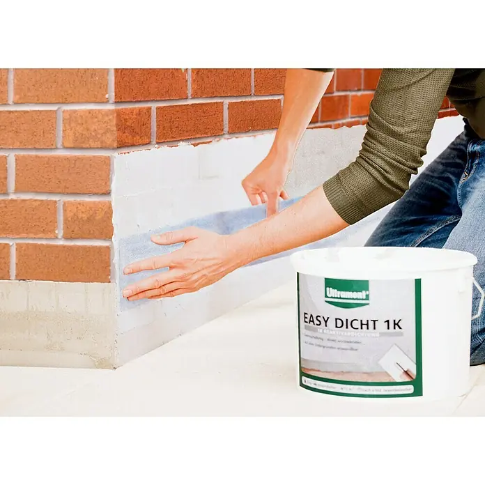 Ultrament Reaktivabdichtung Easy Dicht - 10 kg, 1-komponentig - Ein Handwerker bringt eine Dichtungsbahn an einer Backsteinmauer an, mit einem Eimer Ultrament Easy Dicht 1K im Vordergrund.