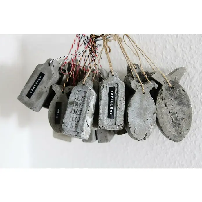 Ultrament Beton-Knetmasse Knet Beton - Hellgrau, 2,5 kg - Eine Nahaufnahme von handgefertigten Betonanhängern in verschiedenen Formen, beschriftet und an einer Schnur aufgehängt.