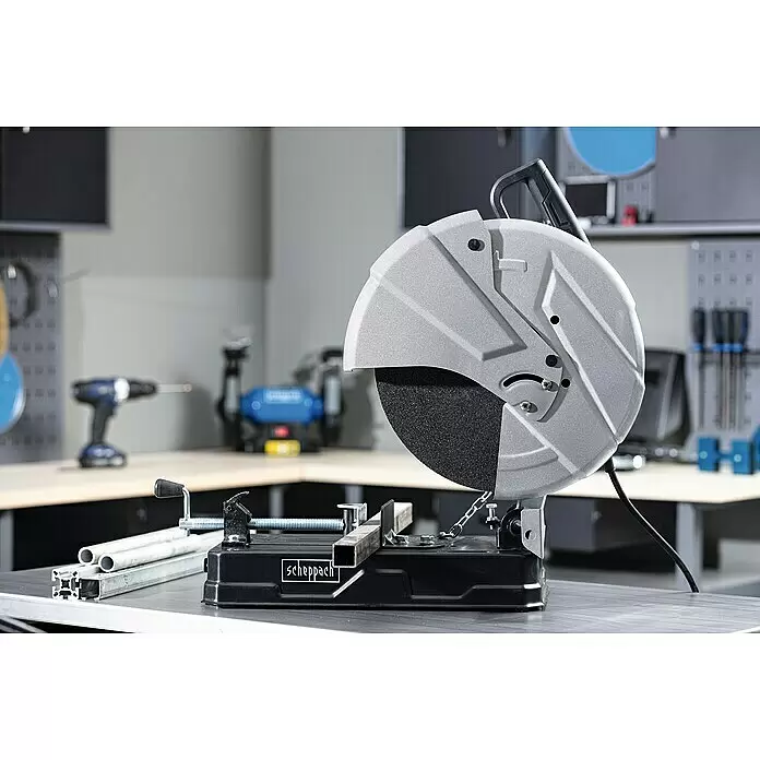 Scheppach Trennschneider MT150 - 2.600 W, Leerlaufdrehzahl: 4.200 U/min, Durchmesser Scheibe: 355 mm - Eine graue und schwarze Trennsäge auf einer Werkbank, die ein quadratisches Metallprofil schneidet. Weitere Metallrohre und -profile liegen in einer Werkstatt daneben.