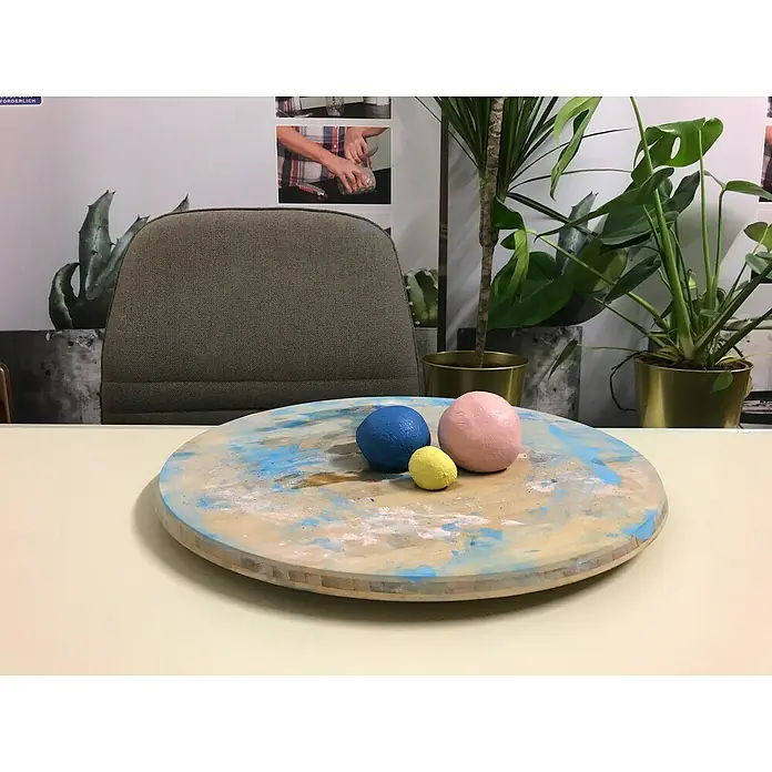 Ultrament Beton-Knetmasse Knet Beton WeissWeiss, 2,5 kg - Nahaufnahme von blauem, gelbem und rosa Ton auf einer bemalten Drehscheibe, die eine spielerische und kreative Atmosphäre suggeriert.