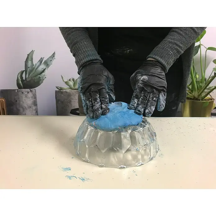 Ultrament Beton-Knetmasse Knet Beton WeissWeiss, 2,5 kg - Hände mit schwarzen Handschuhen formen blaue Modelliermasse in einer transparenten Schale.