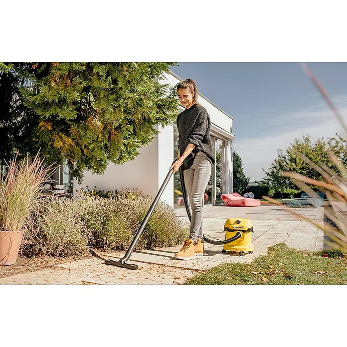 Kärcher Elektro-Nass- & Trockensauger WD 2 PLUS V-12/4/18 - 1.000 W, Behältervolumen: 12 l - Frau reinigt mit einem gelben Kärcher Nass-Trockensauger eine Terrasse im Freien. Das Gerät verfügt über Rollen für einfachen Transport.