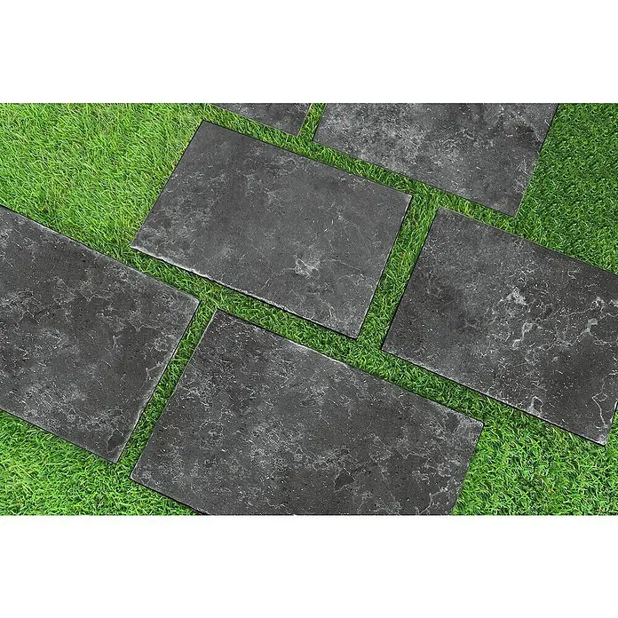 Terrassenfliese Cera 2.0 - 40,8 x 60,1 x 2 cm, Antiquus Carbon, Matt - Ein Gehweg aus dunklen Steinplatten schlängelt sich durch grünes Gras und bietet eine stilvolle und natürliche Gartenweglösung.