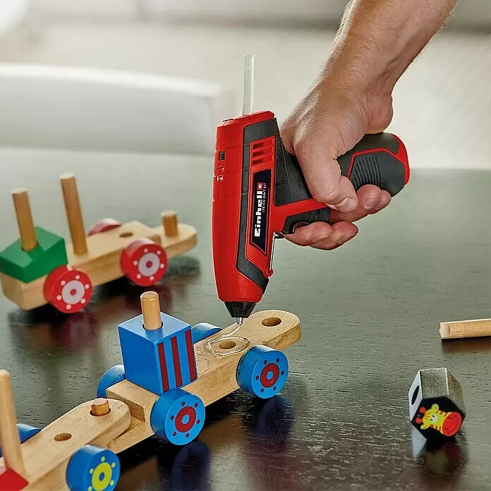 Einhell Klebepatronen - Gesamtstückzahl: 24 Stk., Durchmesser Klebepatrone: 7 mm - Eine Hand benutzt eine rot-schwarze Akku-Heißklebepistole, um Holzspielzeug zu kleben.
