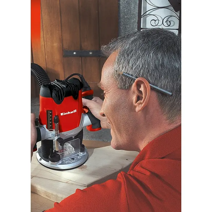 Einhell Fräser-SetDurchmesser Schaft: 8 mm, 15 -tlg. - Nahaufnahme eines Mannes, der mit einer Einhell Oberfräse an einem Holzstück arbeitet, wobei ein Bleistift hinter seinem Ohr steckt.