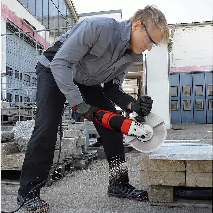 Einhell Diamant-Trennscheiben-Set - Durchmesser Scheibe: 230 mm, 2 -tlg. - Mann verwendet einen rot-schwarzen Winkelschleifer mit silberner Trennscheibe zum Schneiden einer Steinplatte.