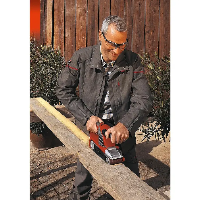 Einhell Schleifband-Set533 x 75 mm, Körnung: 40 - 120, 5 -tlg. - Mann benutzt einen roten Einhell Bandschleifer, um ein Holzbrett zu bearbeiten. Schutzbrille wird getragen.