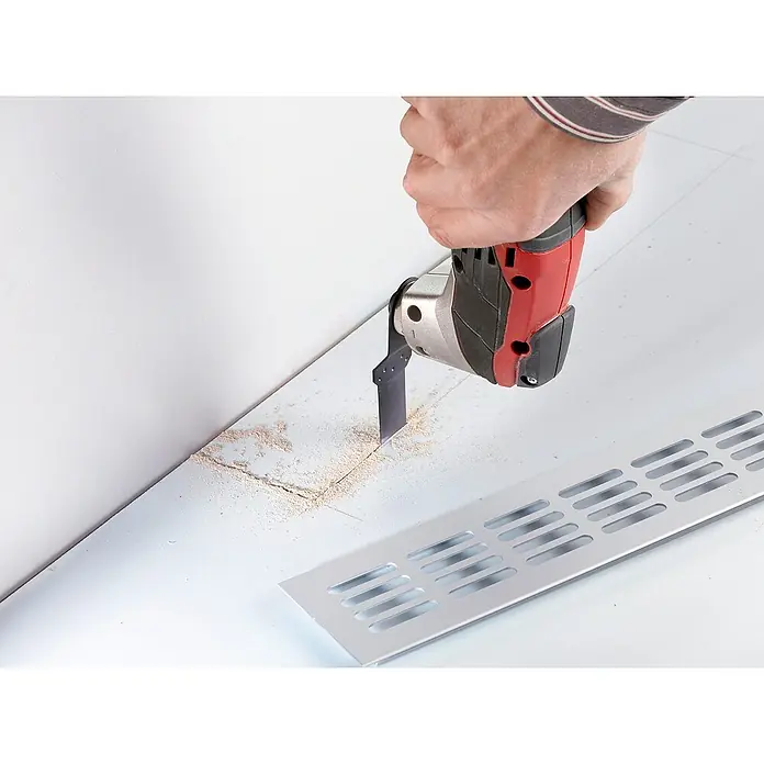 Einhell Zubehör-Set - 4 Stk., 4 -tlg. - Nahaufnahme eines Multitools beim Schneiden von Holz in der Nähe einer Wand und eines Metallgitters.