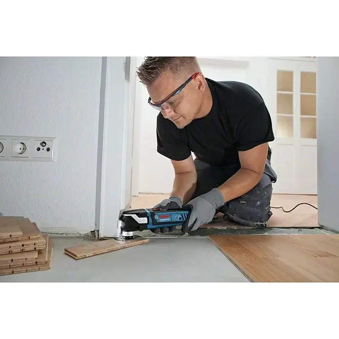 Bosch Professional Multiherramienta GOP 40-30 + accesorios - 400 W, Sistema STARLOCK - Un hombre está arrodillado y utiliza una multiherramienta Bosch para trabajar un trozo de madera.
