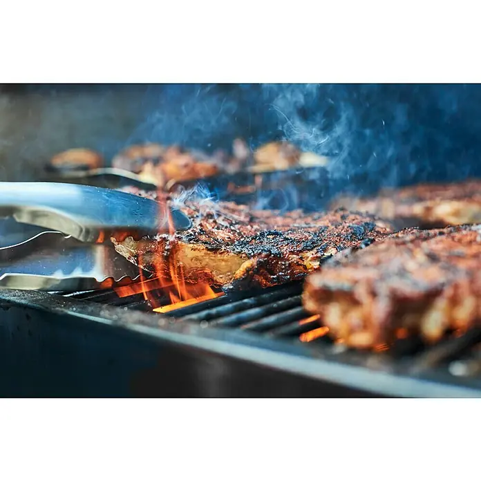 Weber Pelletgrill Smokefire EX4 GBS - Grillfläche (B x T): 61 x 46 cm, Schwarz - Saftige Steaks brutzeln auf dem Grill, während eine Grillzange sie wendet. Rauchentwicklung und Flammen sorgen für ein köstliches Aroma.