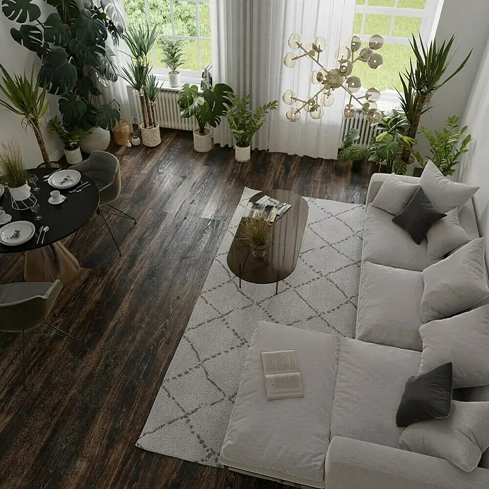 Parkett - Eiche Grindelwald, Landhausdiele, 1.900 x 190 x 15 mm - Ein hellgraues Ecksofa mit Kissen liegt auf einem gemusterten Teppich in einem hellen Wohnzimmer mit Pflanzen und einem Esstisch.