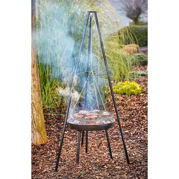 Grillstar Schwenkgrill Louisiana - Durchmesser Grillfläche: 47 cm, Höhe: 160 cm, Schwarz - Ein Dreibein-Grill mit Grillrost und Grillgut steht im Freien. Rauch steigt auf, während das Fleisch brutzelt.