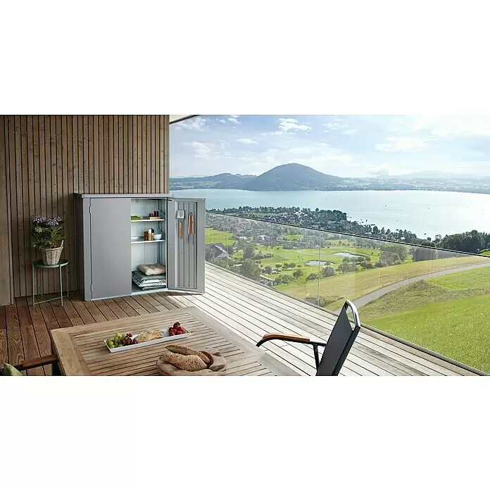 Biohort Romeo Geräteschrank Romeo Gr. M - Außenmaß inkl. Dachüberstand (B x T): 132 x 57 cm, Stahl, Quarzgrau-Metallic - Grauer Metall-Outdoor-Schrank mit geöffneten Türen, der Regale mit Kissen und Grillwerkzeugen auf einer Holzterrasse zeigt.