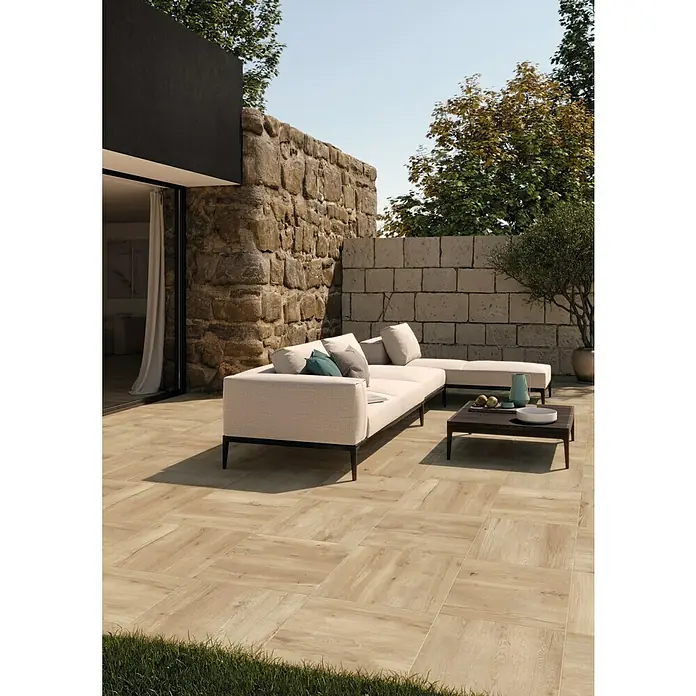 Terrassenfliese Click and Go Ardesia Lignea Rovere - 60 x 60 cm, Eiche, Matt - Eine stilvolle Terrasse mit hellen Holzfliesen, einem bequemen Outdoor-Sofa und einem dunklen Couchtisch, ideal zum Entspannen im Freien.