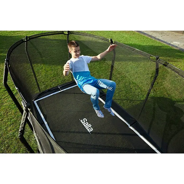 Salta Trampolin Premium Black Edition - 214 x 153 cm, Schwarz - Ein Junge springt auf einem rechteckigen Salta-Trampolin mit Sicherheitsnetz im Garten und hat dabei viel Spaß.