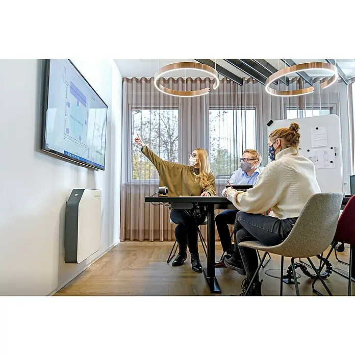 Hönle Luftreiniger SteriWhite Air Q600 - 31,5 x 86 x 86 cm, Wand-/Deckenmontage, Max. Luftleistung: 600 m³/h - Eine Besprechung findet statt mit dem Fokus auf einen großen Bildschirm und einem hellen, tragbaren Luftreiniger an der Wand.