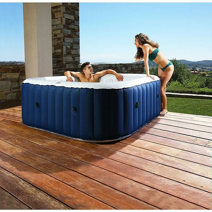 MSpa Mobil-Whirlpool Square Navy - L x B x H: 158 x 158 x 68 cm, Blau, 650 l - Entspannen Sie im aufblasbaren Whirlpool mit blauem Design. Ein Mann sitzt drin, eine Frau steht daneben auf der Holzterrasse.