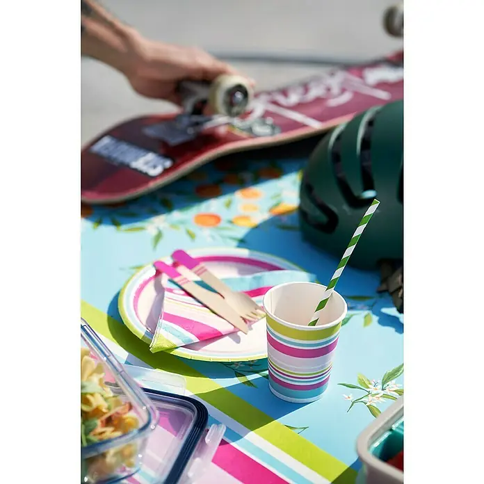 Duni Einwegbecher - 24 cl, Naturmaterialien, Bright Stripes, 10 Stk. - Ein farbenfroher Pappbecher mit grün-weiß gestreiftem Trinkhalm steht auf einem Tisch mit Skateboard und Helm.