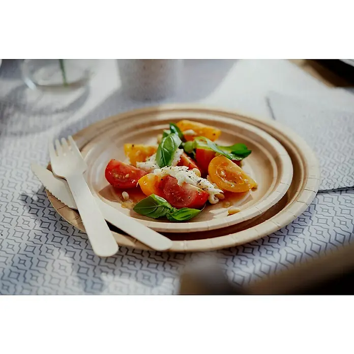 Duni Pappteller Bagasse - 10 Stk., Durchmesser: 18 cm, Zuckerrohrfaser - Ein Teller mit einem Caprese-Salat, bestehend aus Tomaten, Mozzarella und Basilikum, auf einem beigen Pappteller mit Holzbesteck.