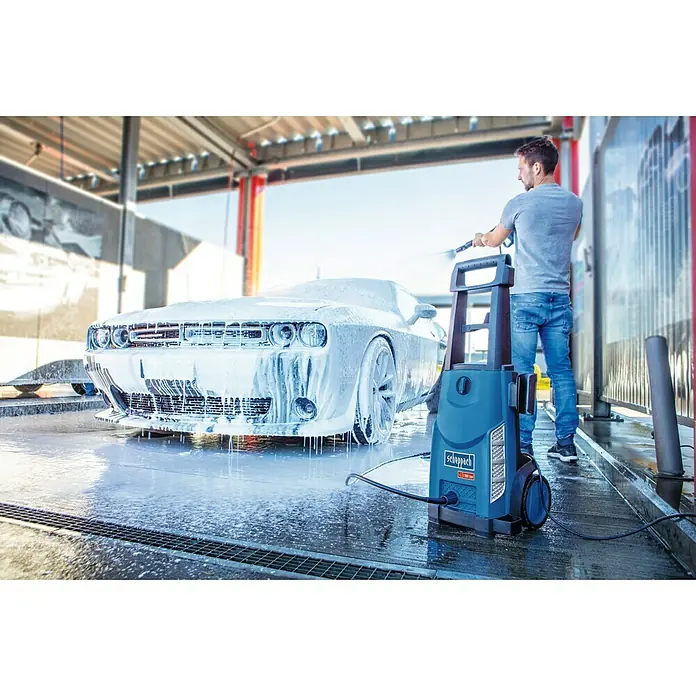 Scheppach Hidrolimpiadora de alta presión HCE 2600 - 180 bar, 2.400 W, Capacidad de bombeo: 480 l/h - Hidrolimpiadora Scheppach en acción: Un hombre limpia un coche cubierto de espuma, con la hidrolimpiadora en primer plano, listo para la próxima tarea.