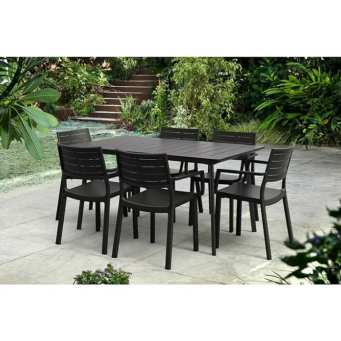 Keter Mesa de jardín Metalea - L x An x Al: 146,5 x 87 x 75 cm, Polipropileno, Marrón - Conjunto de comedor exterior gris oscuro con mesa y sillas en un patio con exuberante vegetación al fondo. Ideal para comidas al aire libre.