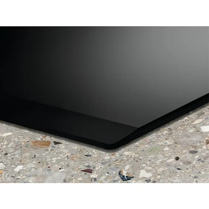 Electrolux Placa de cocción EIV83446 - Número de fogones de inducción: 4 ud. - Primer plano de una elegante placa de cocción vitrocerámica negra sobre una moderna superficie de terrazo, destacando su diseño elegante y materiales de calidad.