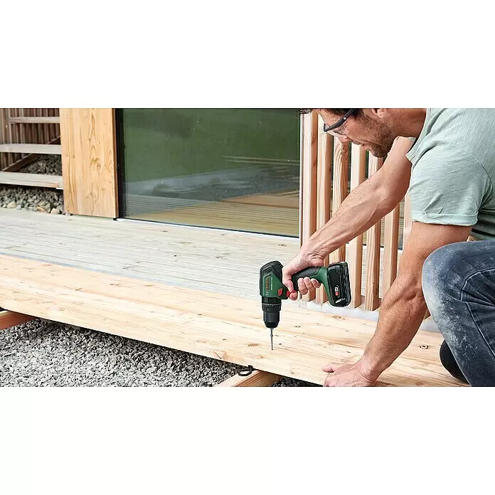 Bosch Power for All 18V Akku-Schlagbohrschrauber UniversalImpact 18V-60 - 18 V, 2 Akkus, 2 Ah, 60 Nm - Mann befestigt eine Holzdiele auf einer Terrasse mit einem grün-schwarzen Bosch Akku-Bohrschrauber.