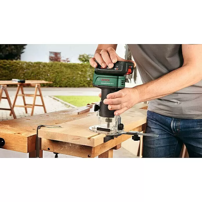 Bosch Power for All 18V Akku-Kombifräse AdvancedTrimRouter 18V-8 - 18 V, Ohne Akku, Leerlaufdrehzahl: 10.000 U/min - 30.000 U/min - Eine Person fräst mit dem grün-schwarzen Bosch AdvancedTrimRouter 18V-8 präzise eine Nut in helles Holz an einer Werkbank.