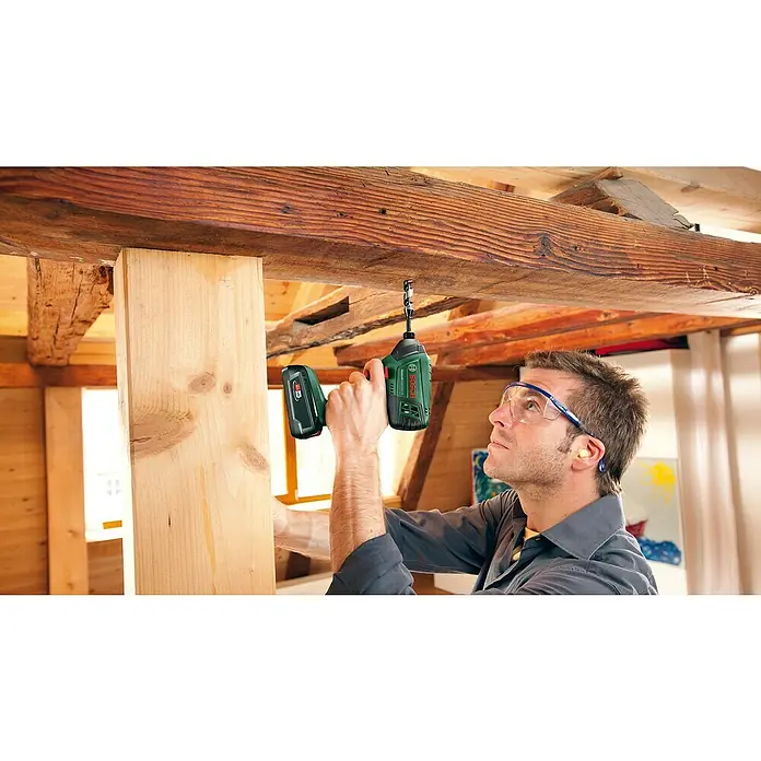 Bosch Power for All 18V Akku-Schlagbohrschrauber AdvancedImpactDrive 18 - 18 V, Ohne Akku, 130 Nm - Ein Mann befestigt ein Holzstück mit einem grünen Bosch Akku-Schlagschrauber an einer Holzbalkendecke. Er trägt dabei eine Schutzbrille.
