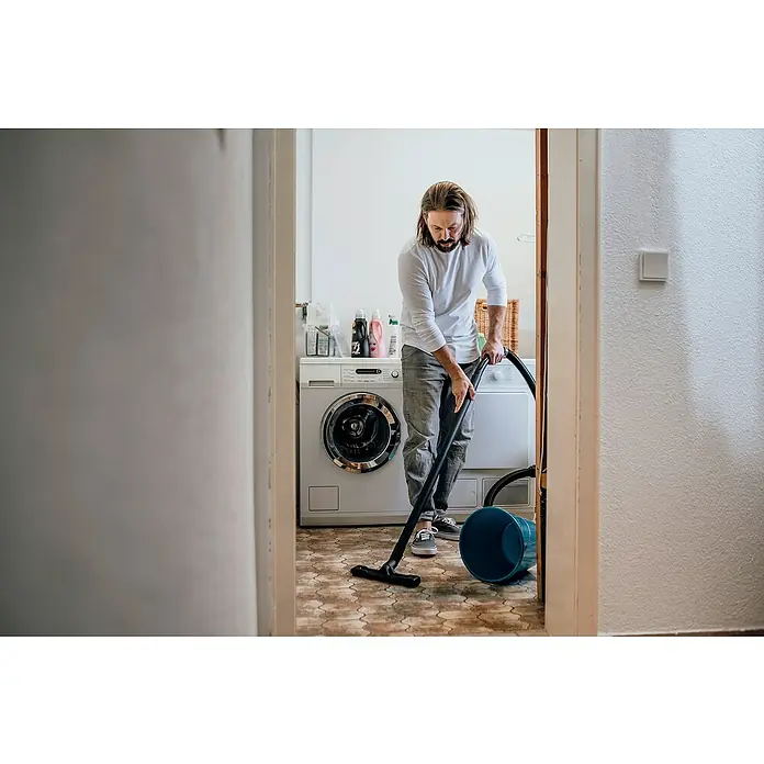 Kärcher Elektro-Nass- & Trockensauger WD 3 P V-17/4/20 Extension - 1.000 W, 17 l, 9 -tlg. - Ein Mann saugt mit einem Staubsauger den Boden eines Waschraums mit Fliesenmuster. Im Hintergrund befinden sich Waschmaschine und Trockner.