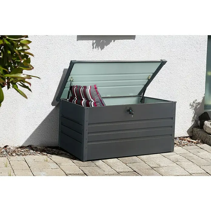 Gardol Garten-Aufbewahrungsbox - L x B x H: 132 x 62 x 62 cm, Anthrazit, Metall - Eine graue Gartenbox mit geöffnetem Deckel und einem gestreiften Kissen darin, die auf einer gepflasterten Fläche vor einer Wand steht.