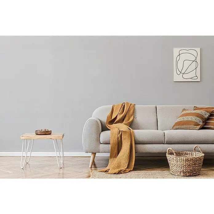 Erfurt Vliestapete Variovlies Sand - Weiß, Uni, 25 x 0,75 m - Ein minimalistisches Wohnzimmer mit einem grauen Sofa, einer warmen Decke und einem kleinen Holztisch, das ein gemütliches Ambiente schafft.