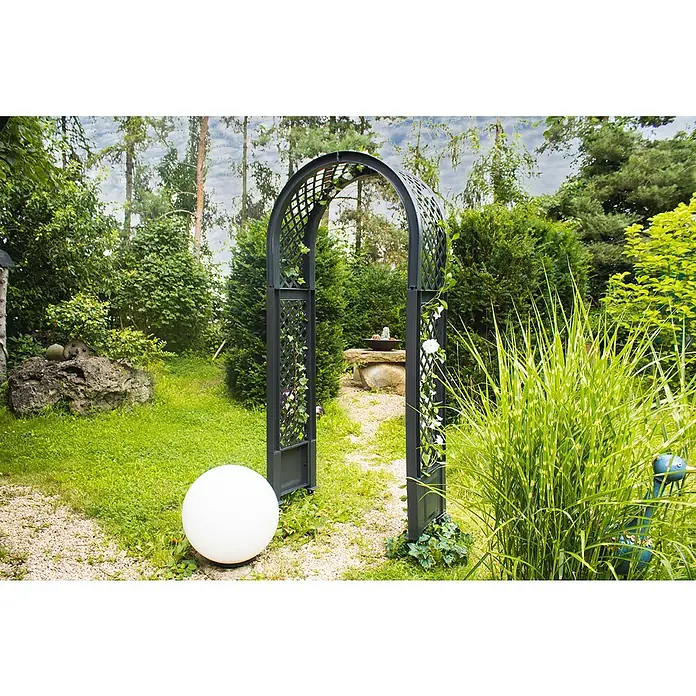 KHW Rosenbogen - Anthrazit, 100 x 43 x 207 cm - Ein dekorativer Gartenbogen aus Metall mit Kletterpflanzen steht auf einem Kiesweg in einem üppigen Garten, neben einem weißen Dekoball.