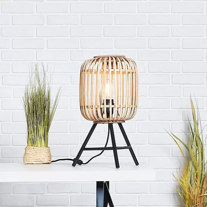 Brilliant Woodrow Tischleuchte - Hellbraun, E27, 60 W - Tischlampe aus Holzlamellen mit schwarzen Stativbeinen auf weißem Tisch, neben Zierpflanzen.
