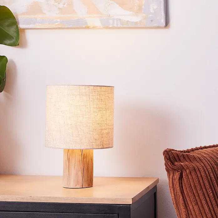 Brilliant Pia Tischleuchte - 40 W, Holz, E27 - Nahaufnahme einer Nachttischlampe mit einem Lampenfuß aus Holz und einem Lampenschirm aus Stoff, die eine warme und gemütliche Atmosphäre schafft.