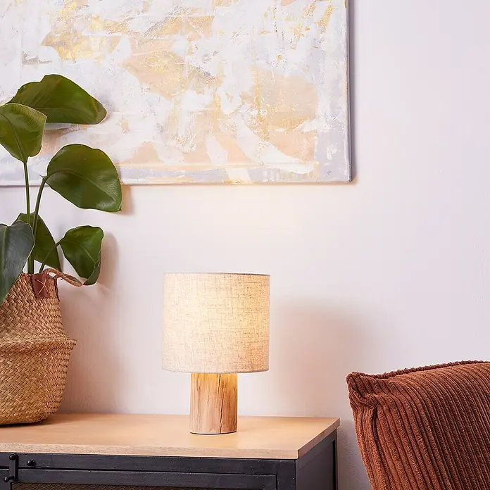 Brilliant Pia Tischleuchte - 40 W, Holz, E27 - Nahaufnahme einer stilvollen Nachttischlampe mit einem Lampenfuß aus Holz und einem Textilschirm, die ein warmes Licht ausstrahlt.