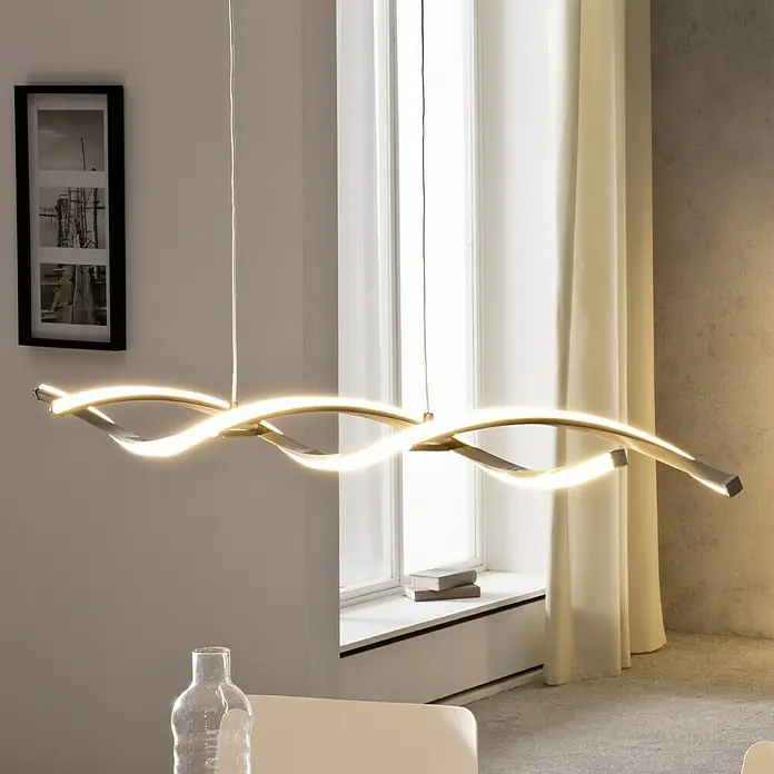 Paul Neuhaus Polina LED-Pendelleuchte - Warmweiß - Eine moderne LED-Pendelleuchte mit geschwungenem Design hängt über einem Tisch und sorgt für elegante Beleuchtung im Raum.