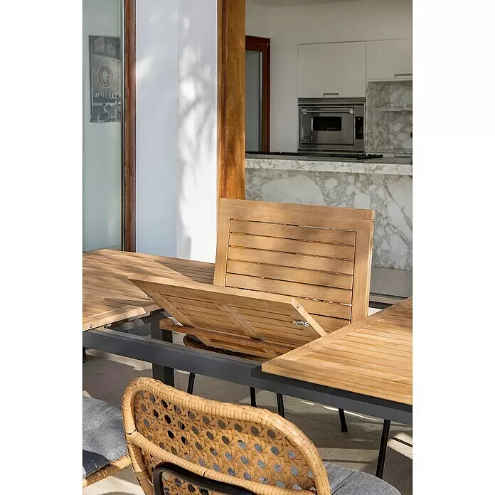 Sunfun Carina Gartentisch - L x B x H: 180 x 100 x 75 cm, Akazie, Stahl, Rechteckig, Hellbraun - Ausziehbarer Lamellen-Holztisch für den Außenbereich mit dunkelgrauem Rahmen wird ausgezogen, daneben ein geflochtener Korbsessel mit grauem Kissen.