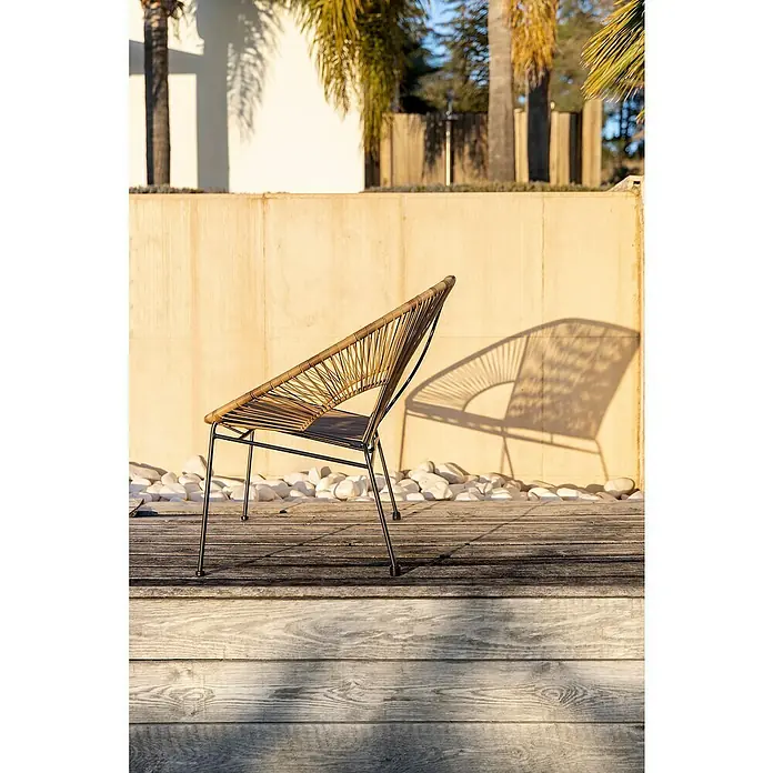 Sunfun Sillón de jardín Fidji - Marrón - Primer plano de una silla de ratán con patas metálicas sobre una pared amarilla clara y piedras blancas.