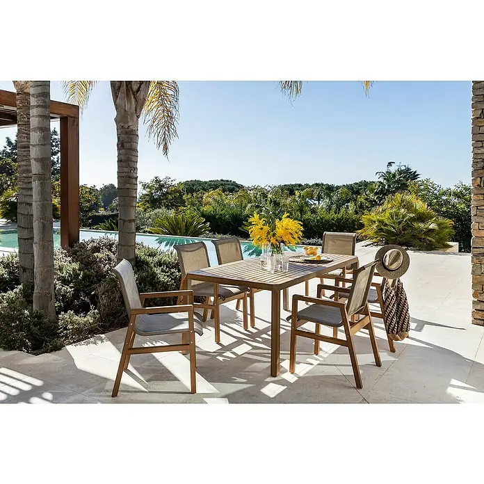 Conjunto de muebles Flavium - 7 pzs., Textiline/Enviro Imitation Wood®, Natural - Una mesa de jardín con sillas en una terraza, decorada con flores y limones, con palmeras y piscina al fondo.