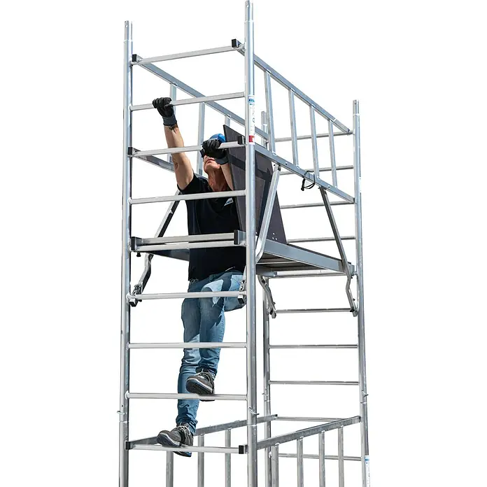 Krause ProTec RollgerüstArbeitshöhe: 11,3 m, Bühnengröße: 2 x 0,6 m, Belastbarkeit: 200 kg/m² - Ein Mann klettert auf einem KRAUSE Fahrgerüst mit einer Arbeitsplattform und Geländern, um Arbeiten in der Höhe sicher durchzuführen.