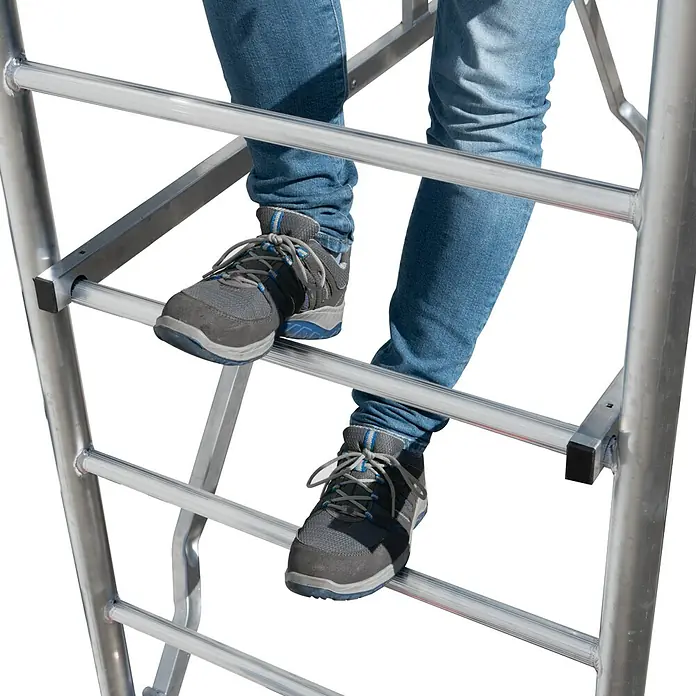 Krause ProTec RollgerüstArbeitshöhe: 11,3 m, Bühnengröße: 2 x 0,6 m, Belastbarkeit: 200 kg/m² - Eine Person steigt auf einer Aluminiumleiter mit grauen Schuhen und blauen Jeans.