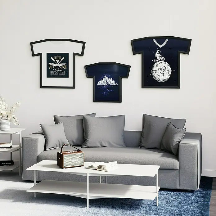 Umbra Bilderrahmen Trikot - 62 x 72 cm, Schwarz - Eine moderne Wohnzimmergestaltung mit T-Shirt-Kunstdrucken an der Wand, einem grauen Sofa und einem weißen Couchtisch.